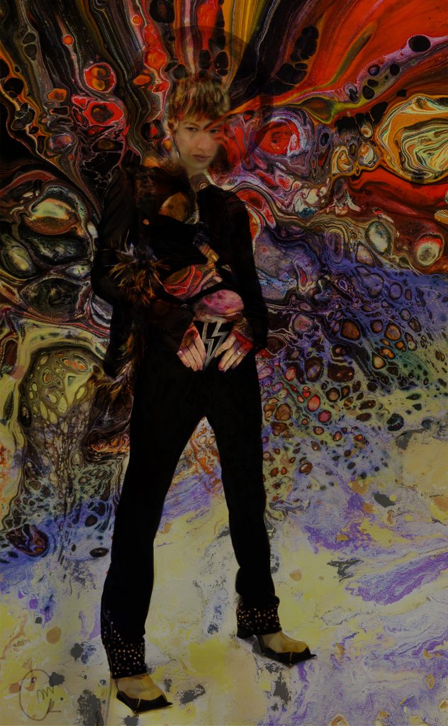 Chico con escafranda, pendiente grande de flecha, cinturón de rallo, en fondo abstracto, vestido de negro.